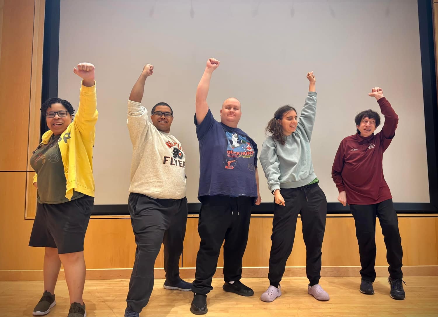 Five CreatAbility students standing side by side on stage with one arm raised in the air, laughing at the end of a scene.