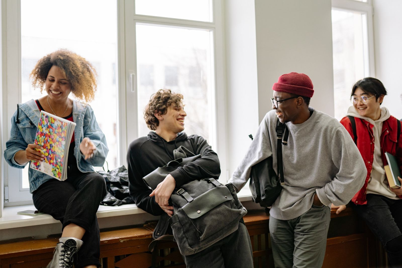 Four adults chatting and laughing together beside a large window, including a wheelchair user.